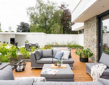Zithoek in de tuin met border van groene planten, houten planken, grijze loungeset