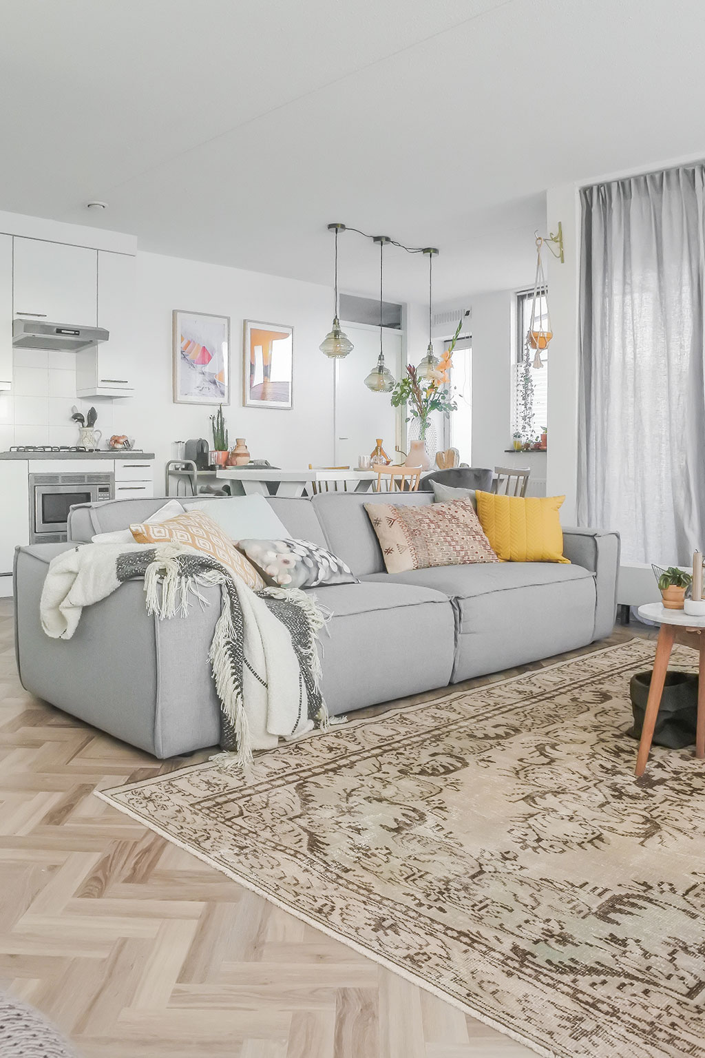 Lichte woonkamer met lichtgrijze bank, visgraatvloer, perzisch vloerkleed in beige en bruin. 