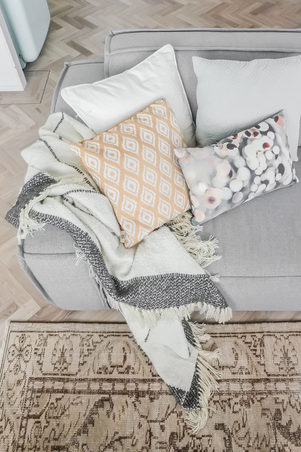 Lichtgrijze bank gestyled met kussens in perzik tint en grafisch blauw. 