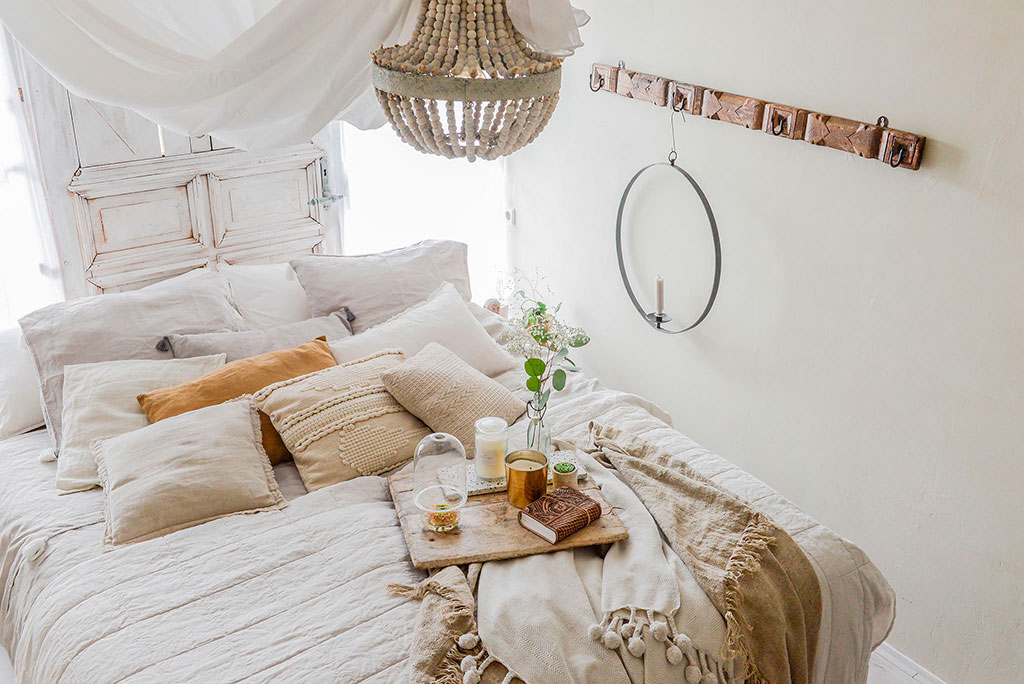 Bohemian style slaapkamer met veel lagen kussens en beddengoed, aardetinten, oude deur als headboard en rotan hanglamp. 