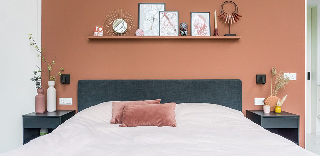 Terracotta muur in slaapkamer met een plankje boven het boxspring bed.