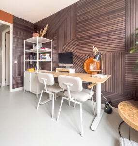 Thuiswerkplek in een aparte ruimte ingericht met een mooi graitsch donkerbruin behang en een wit bureau met houten blad en 2 witte bureaustoelen.