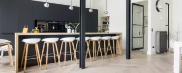 Een verbouwd kantoor tot prachtig woonhuis met een grote open keuken in het zwart met een houten bar met 8 barkrukken