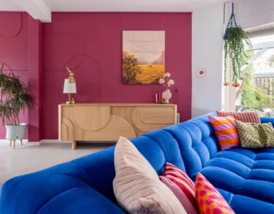 Warme en koele tinten combineren: aubergine op de wand en een kobaltblauwe velvet bank.