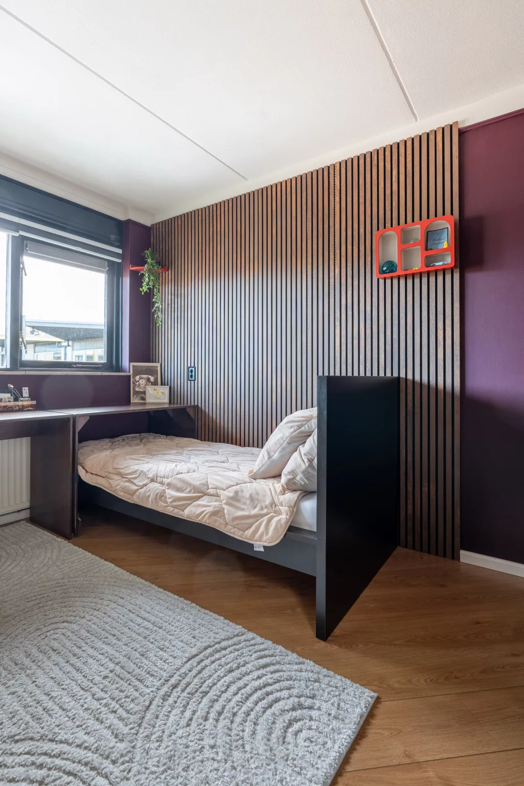 Donker houten lattenwand met aubergine kleurige muur, zwart bed. 