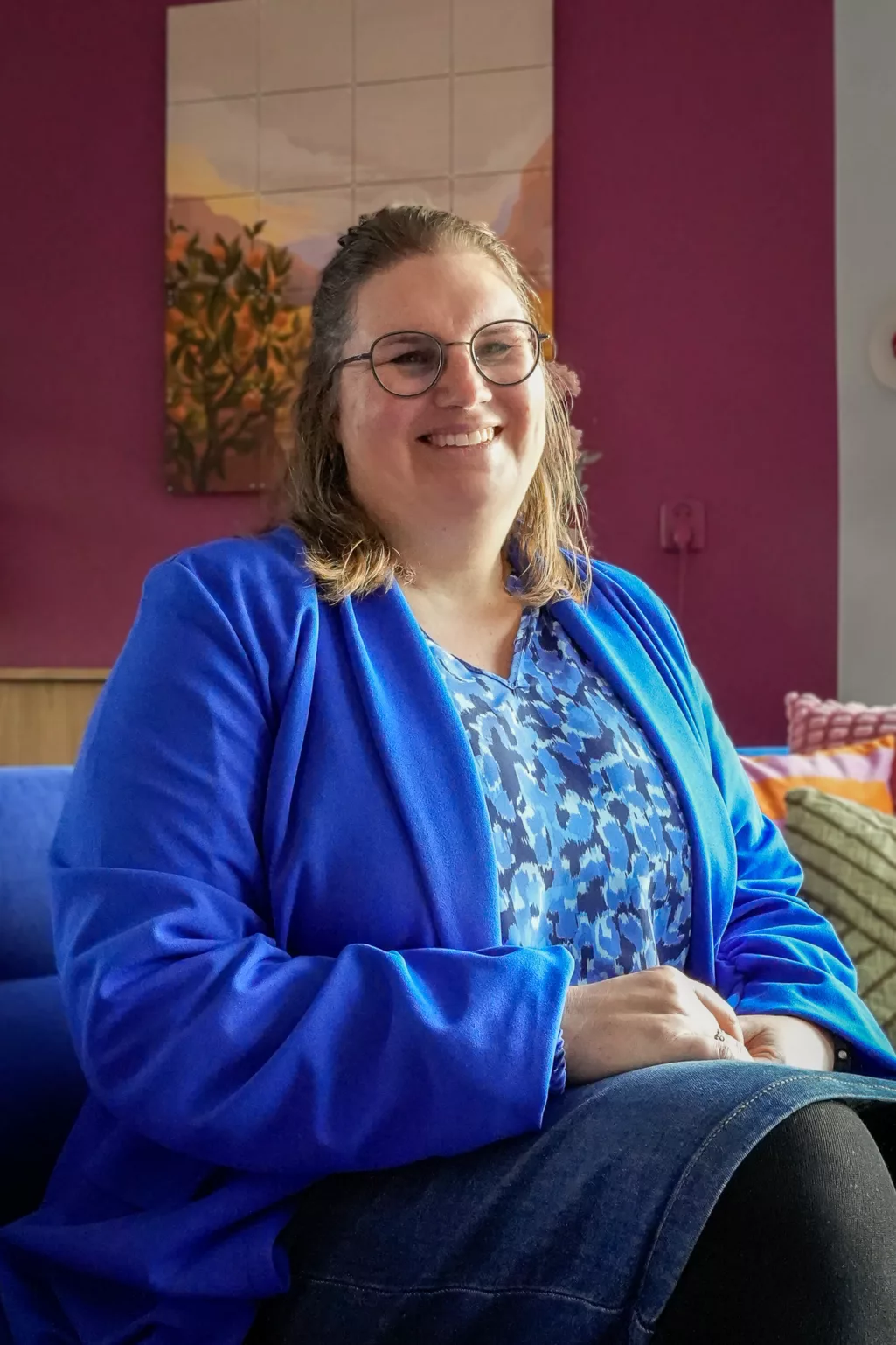 Margriet poseert in een kobaltblauw jasje wat matcht met haar kobaltblauwe bank. 