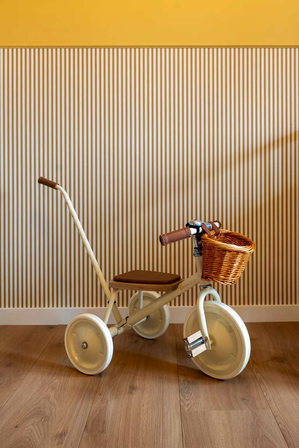 Retro kinderfiets in kinderkamer, streepjesbehang, geel en wit, houten plankenvloer