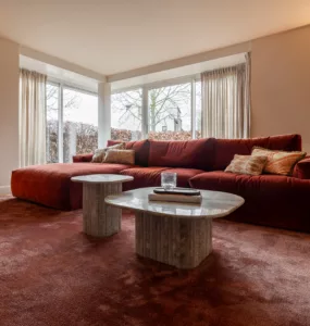 Bordeaux rode hoekbank, bordeaux rood vloerkleed, marmeren salontafels, beige wanden