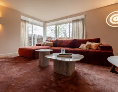 Bordeaux rode hoekbank, bordeaux rood vloerkleed, marmeren salontafels, beige wanden