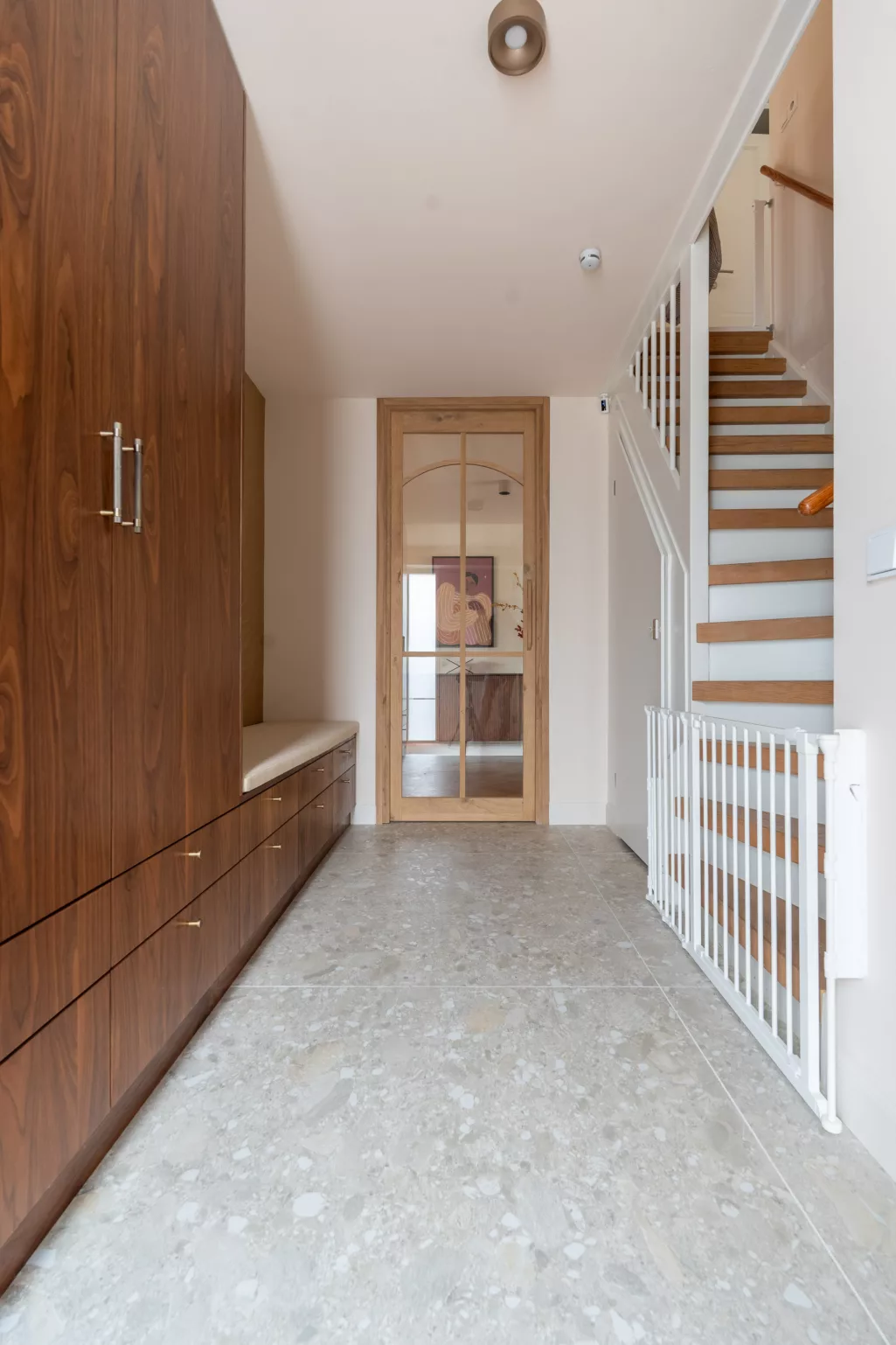 Lichte hal, terrazzo vloer, walnoot houten maatwerkkasten tot plafond, witte trap met houten treden, eiken houten deur met glas tot plafond
