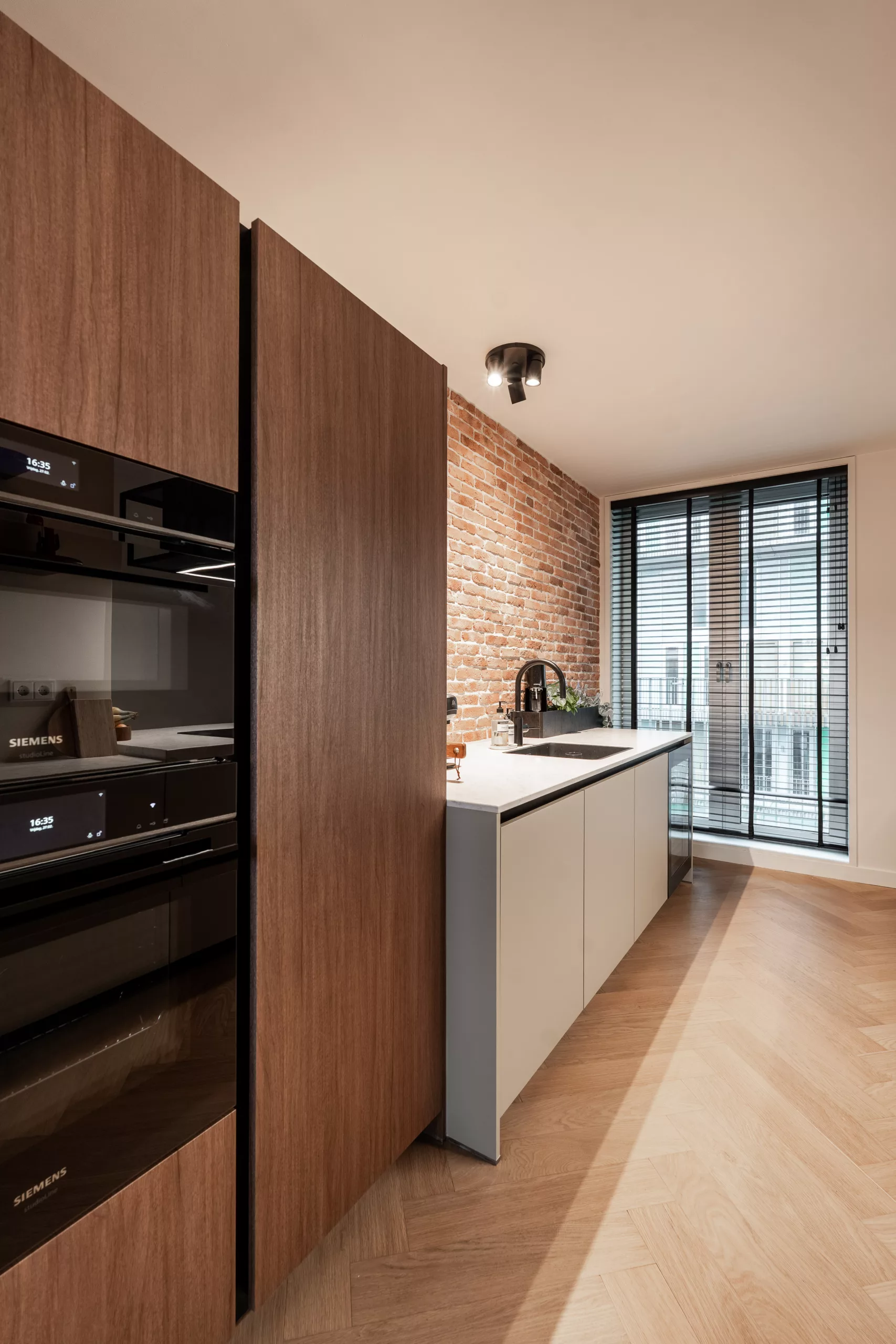 Open keuken met hoge donker houten kasten, zwart inbouwapparatuur, bakstenen muur