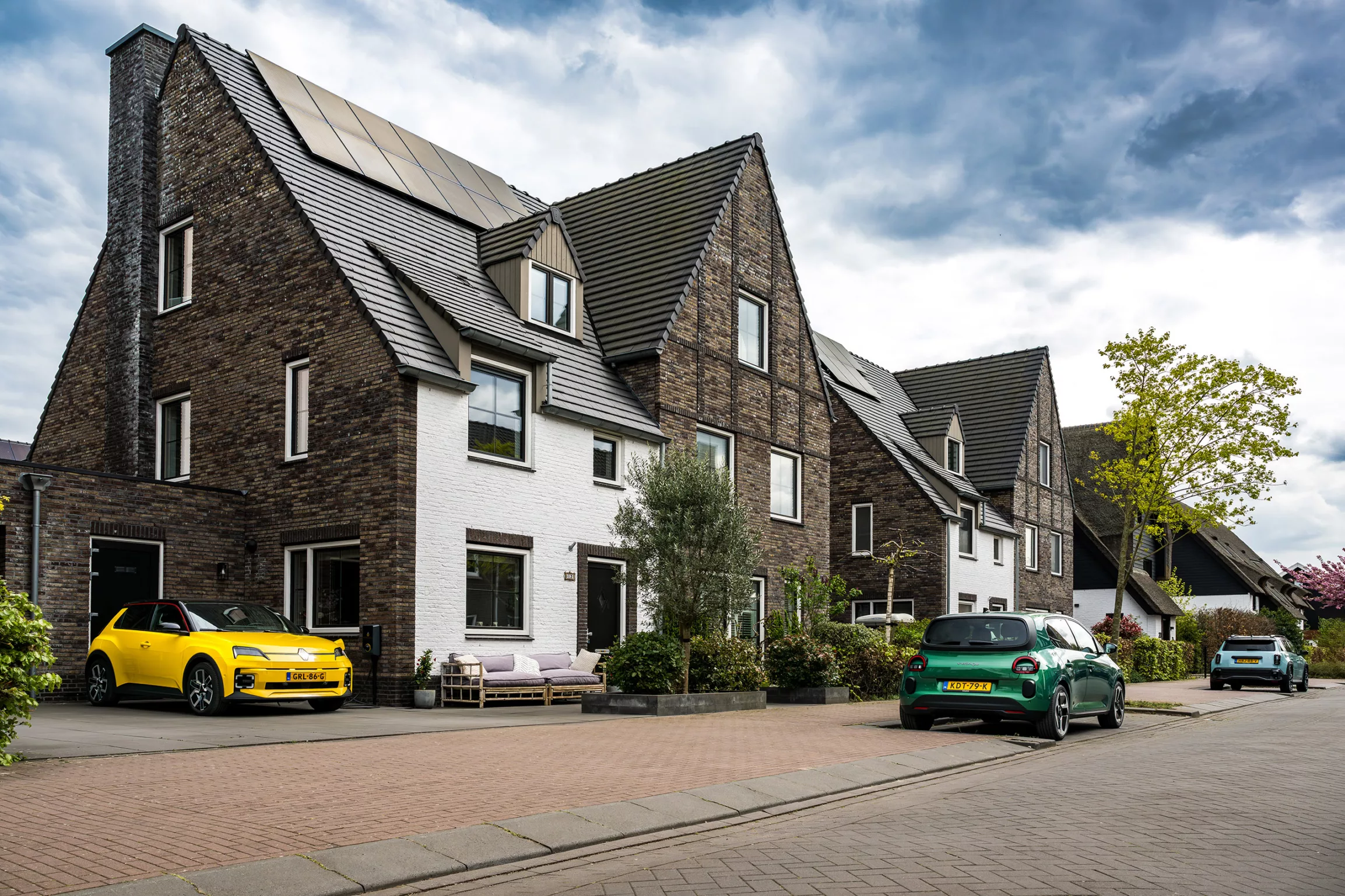 Buitenkant nieuwbouwwoning met Renault Clio op de oprit aan de laadbaal, bruin huis met witte voorkant, zonnepanelen op het dak