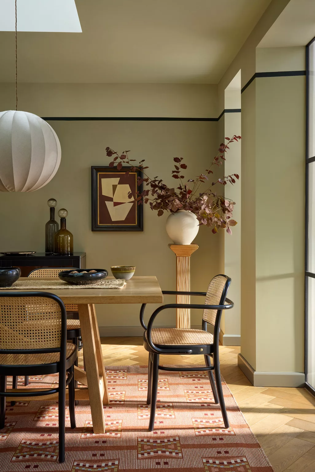 Eethoek in groen salie kleur wanden met 1 tint donkere plinten, rotan stoelen