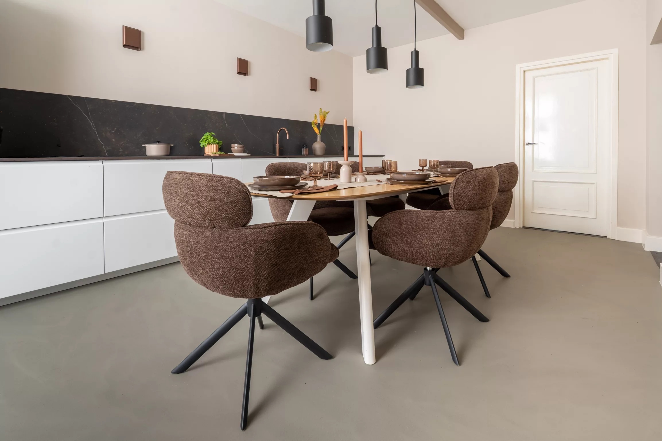 Woonkeuken, ovalen tafel, donkerbruine eetkamerstoelen, beige wanden, donkere glanzende wandlampen, Kelya dekton blad, witte kastjes