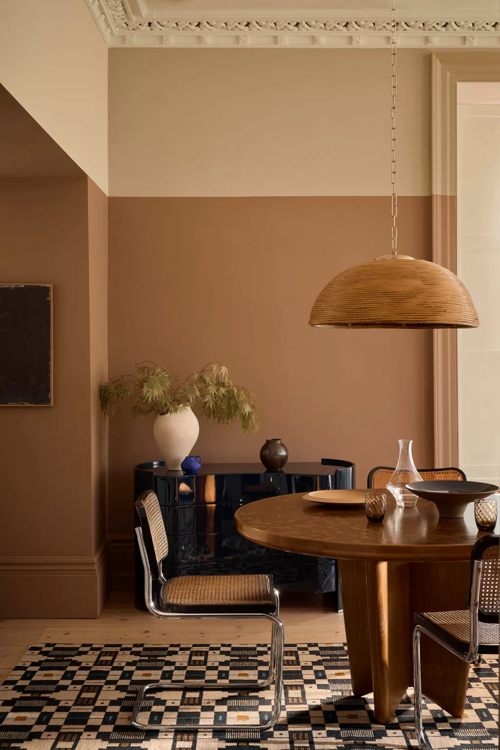 Eethoek met aardetinten, plinten meegeverfd in aardekleur, koperkleurige ronde tafel, zwart met rieten stoelen, rvs onderstel