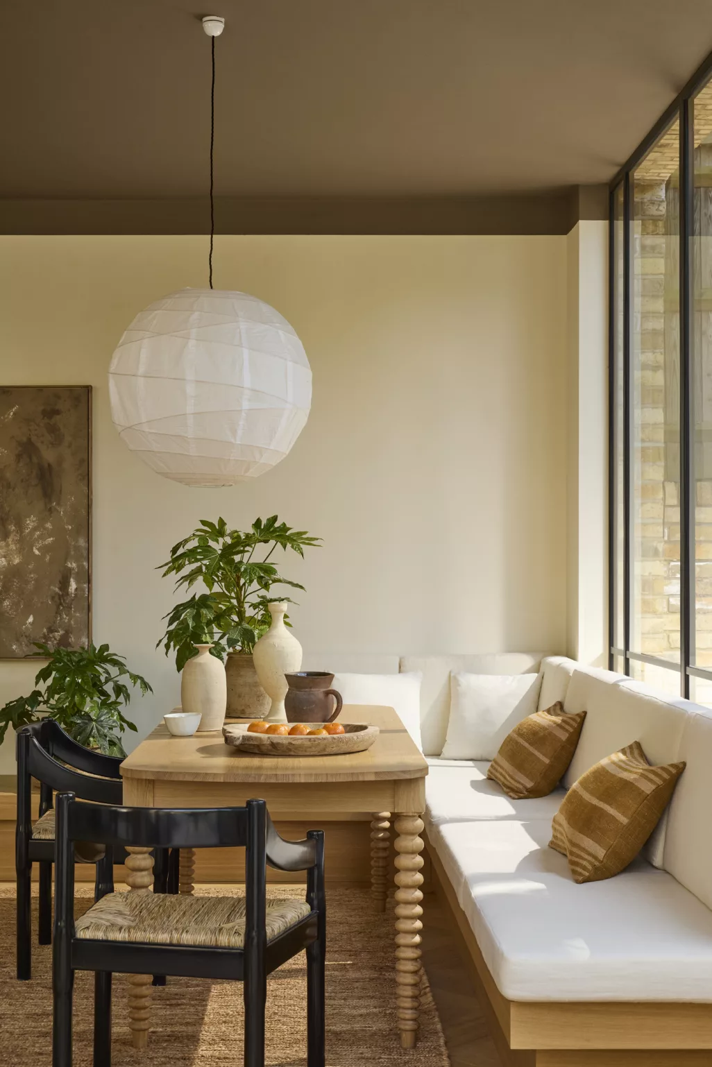 Woonkamer in aardetinten, beige wand, bruin plafond, houten eettafel, zwart met rieten stoelen